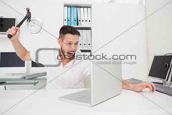 Casual businessman holding hammer over laptop