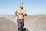Active shirtless senior man jogging on the pier