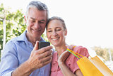 Happy senior couple looking at smartphone holding shopping bags