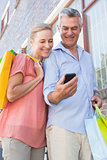 Happy senior couple looking at smartphone holding shopping bags