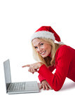 Festive blonde smiling at camera and pointing to laptop