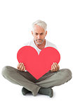 Upset man sitting holding heart shape