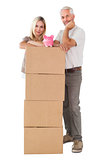 Happy couple leaning on pile of moving boxes with piggy bank
