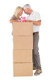 Happy couple leaning on pile of moving boxes with piggy bank