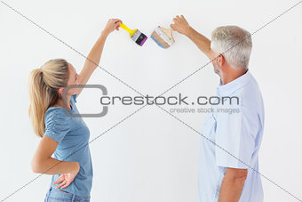 Happy couple painting wall with paintbrushes