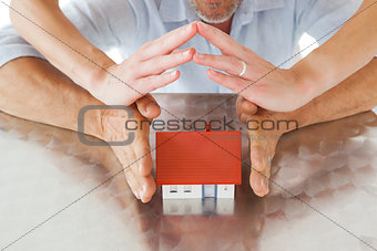 Couple sheltering miniature house with hands