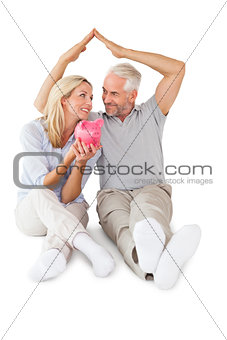 Happy couple sitting and sheltering piggy bank