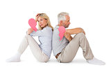 Unhappy couple sitting holding two halves of broken heart