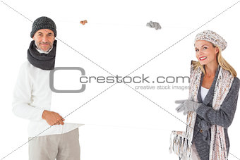 Smiling couple in winter fashion holding poster