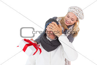 Happy woman holding gift while covering husbands eyes