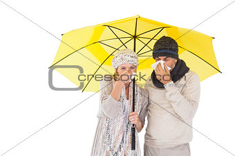 Couple in winter fashion sneezing under umbrella