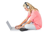 Pretty young blonde sitting using laptop listening to music
