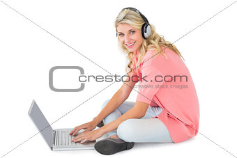Pretty young blonde sitting using laptop listening to music