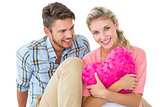 Attractive young couple sitting holding heart cushion
