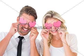 Attractive young couple holding pink hearts over eyes