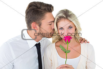 Handsome man kissing girlfriend on cheek holding a rose