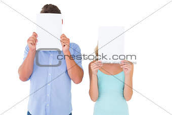 Young couple holding pages over their faces