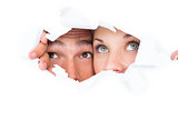 Young couple peeking through torn paper