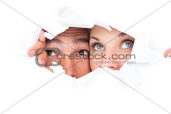 Young couple peeking through torn paper