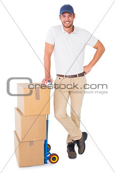 Happy delivery man leaning on trolley of boxes