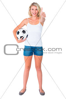 Pretty blonde football fan holding ball showing thumbs up