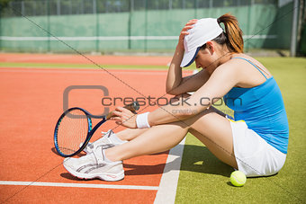 Upset tennis player sitting on court