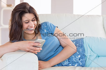 Pretty brunette sending a text on the couch