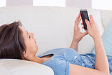 Pretty brunette sending a text on the couch