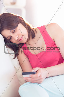 Pretty brunette relaxing on the couch using smartphone