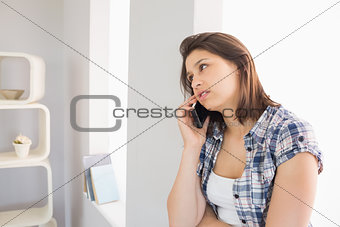 Pretty brunette sitting beside her window talking on phone