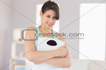 Fit brunette smiling at camera holding scales
