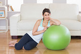 Fit brunette leaning on exercise ball smiling at camera