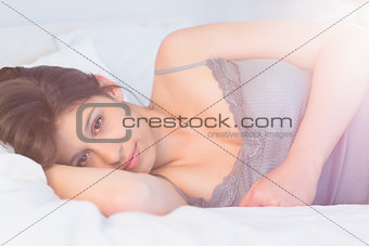 Beautiful brunette lying on bed smiling at camera