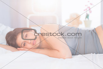 Beautiful brunette lying on bed smiling at camera