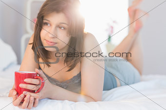 Beautiful brunette lying on bed holding mug