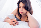 Beautiful brunette using smartphone on bed