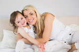 Portrait of happy mother and daughter sitting on bed