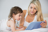 Mother and daughter using digital tablet on bed