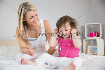 Mother looking at daughter with headphones on bed