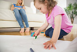 Girl drawing in the living room with mother sitting behind