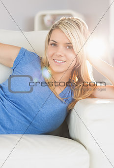 Smiling young woman lying on sofa in living room
