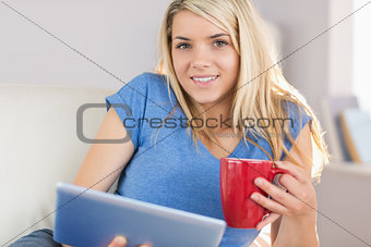 Beautiful woman using digital tablet while drinking coffee at home