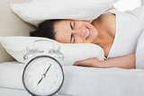 Woman covering ears with pillow in bed