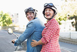 Happy mature couple riding a scooter in the city