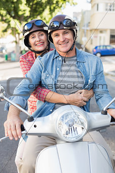 Happy mature couple riding a scooter in the city