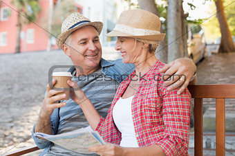 Happy tourist couple drinking coffee on a bench in the city