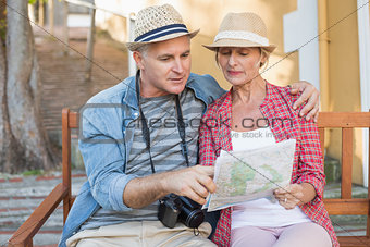 Happy tourist couple looking at map on a bench in the city