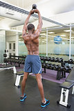 Shirtless muscular man lifting kettle bell in gym