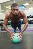 Determined man doing push ups with ball in gym