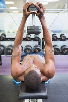 Shirtless man exercising with dumbbell in gym
